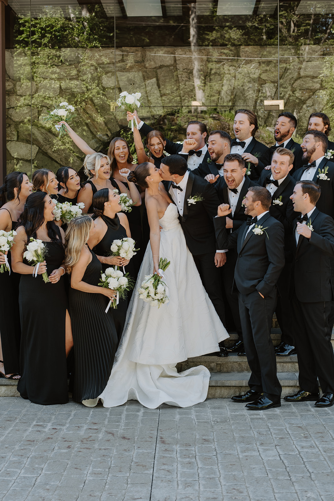 Bride and groom sharing a kiss while their wedding party cheers enthusiastically on the steps.
